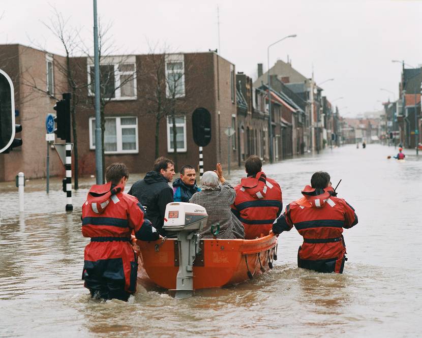 Reddingsverwerkers vervoeren een vrouw in een rubberboot door een overstroomde straat